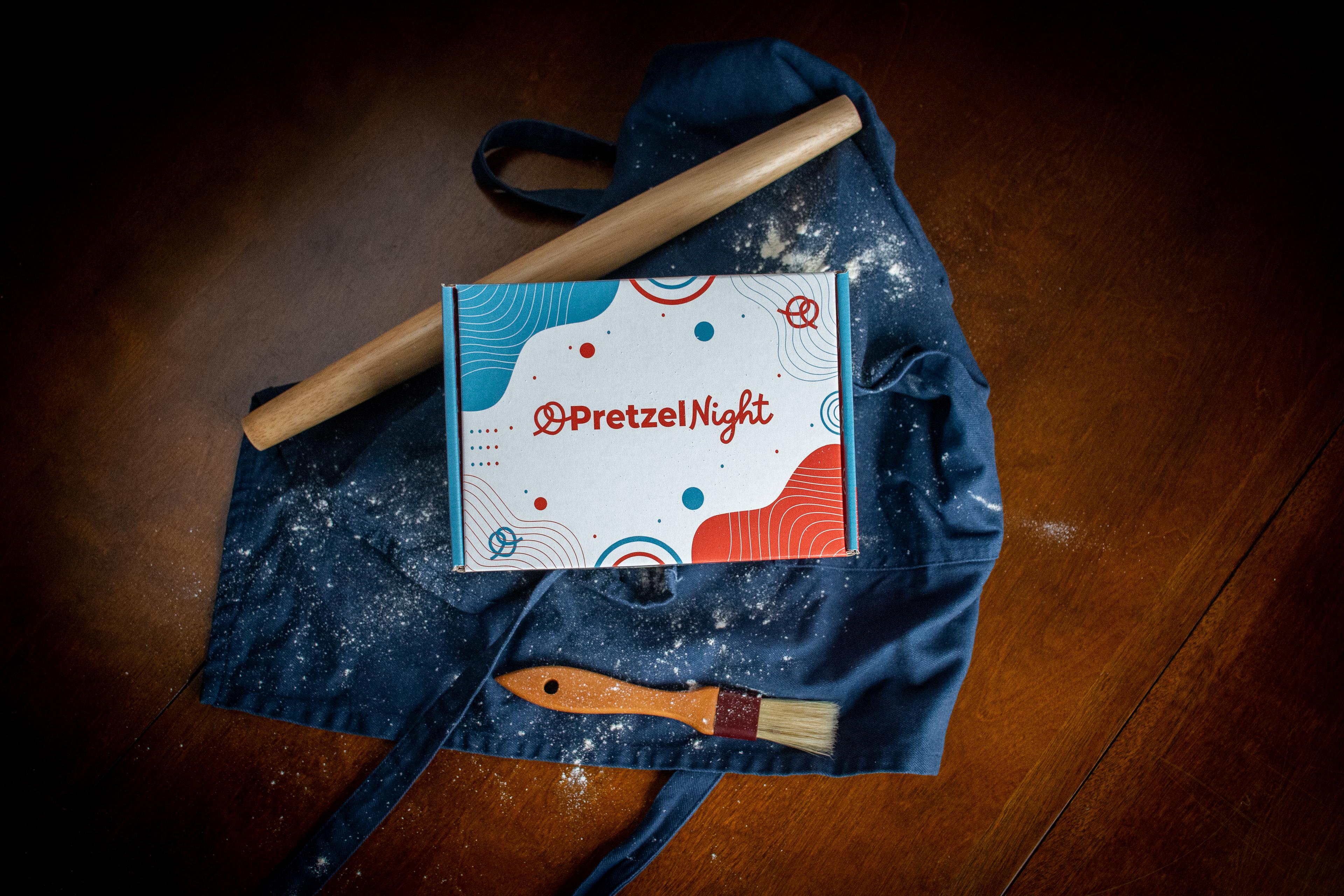 Image that shows the prezel night box on top of an apron with a rolling pin next to it and a brush